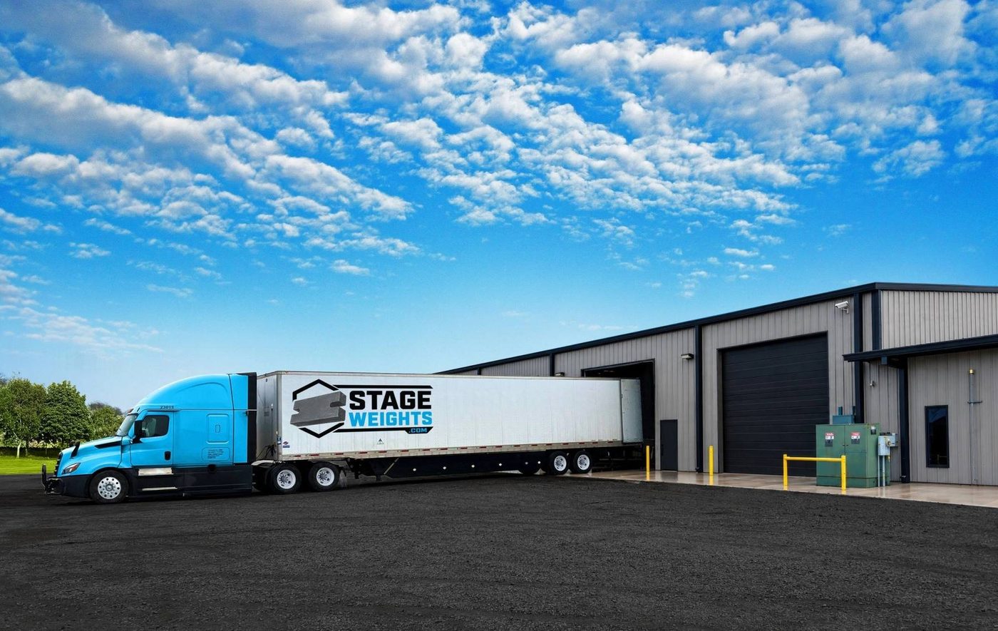 A Stage Weights semi trailer backed up to the loading dock of a steel warehouse under a blue sky